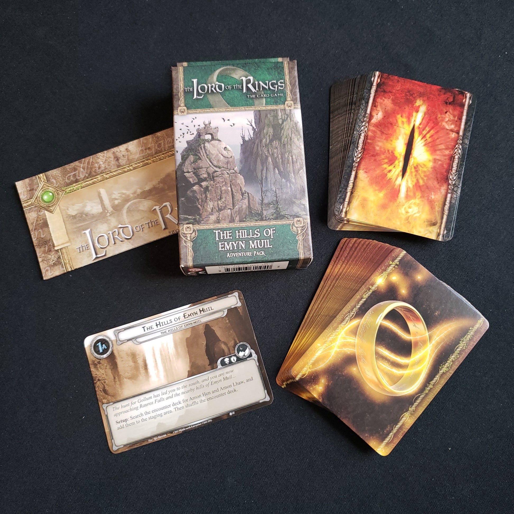 Image shows the front of the package for the Hills of Emyn Muil Adventure Pack for the Lord of the Rings card game, with the cards and instructions fanned out around it