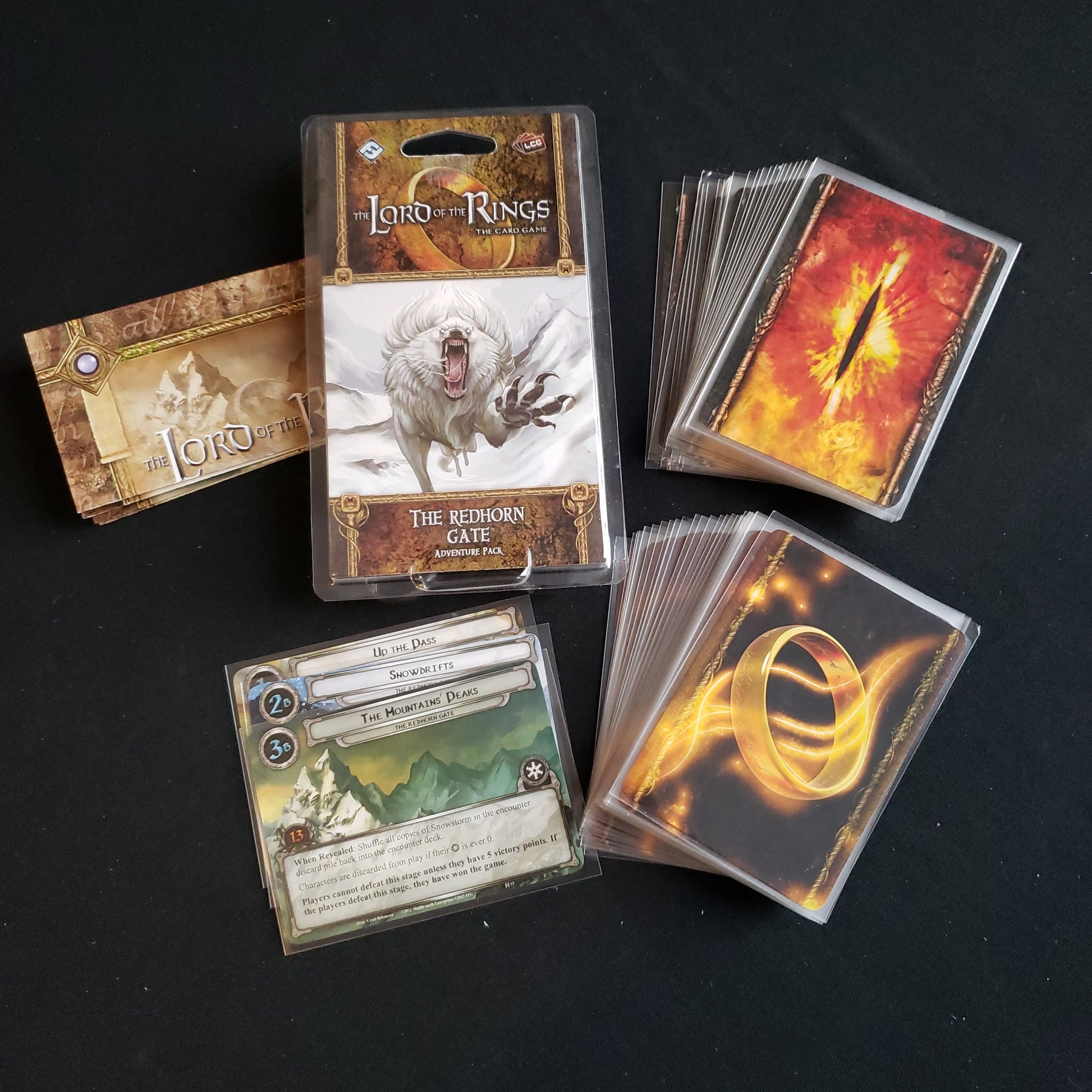 Image shows the front of the package for the Redhorn Gate Adventure Pack for the Lord of the Rings card game, with the cards and instructions fanned out around it