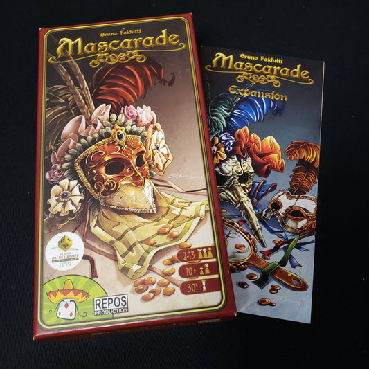 Image shows the front cover of the box of the Mascarade card game sitting n top of the instructions for the expansion