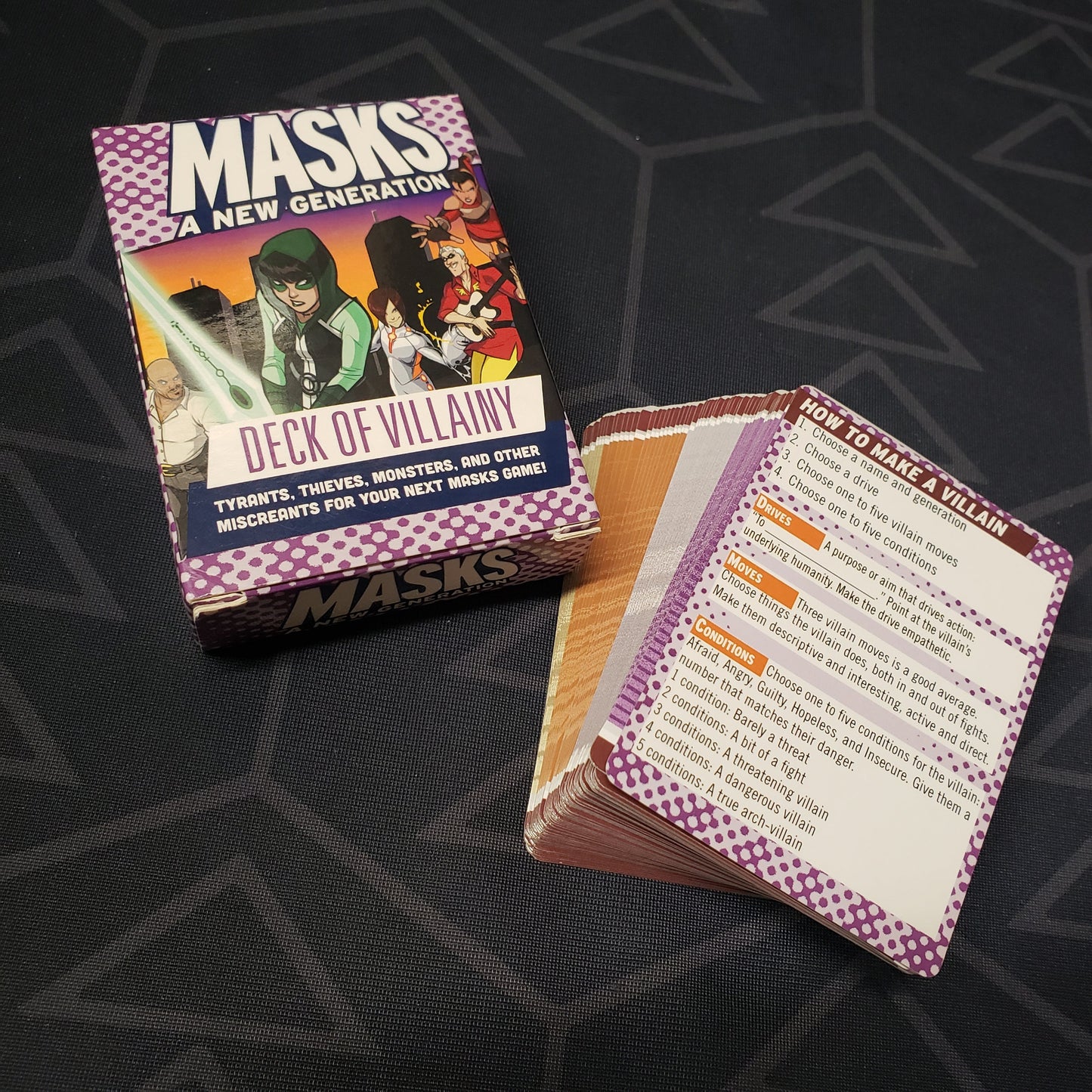 Image shows the front cover of the Deck of Villainy box for the roleplaying game Masks: A New Generation with the cards fanned out next to it