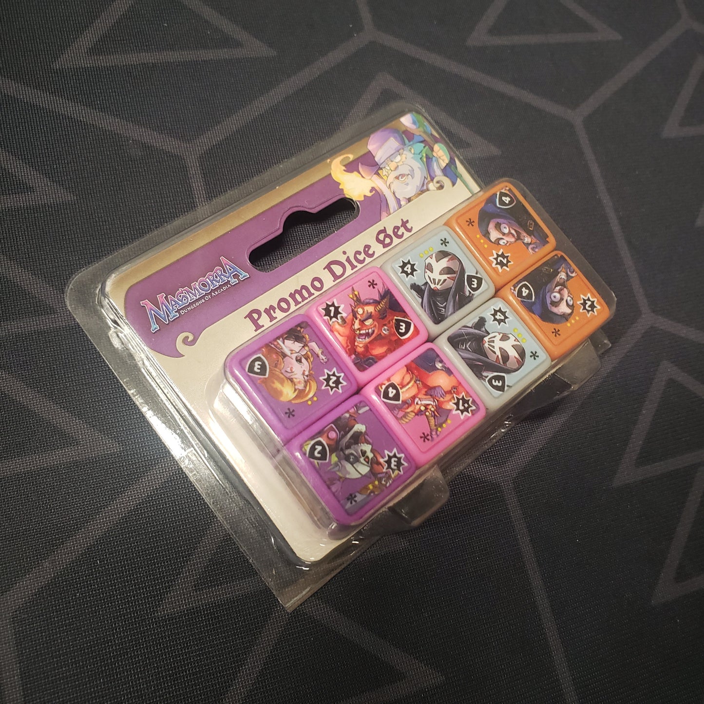 Image shows the front of the packaging of the Promo Dice Set for the board game Masmorra: Dungeons of Arcadia