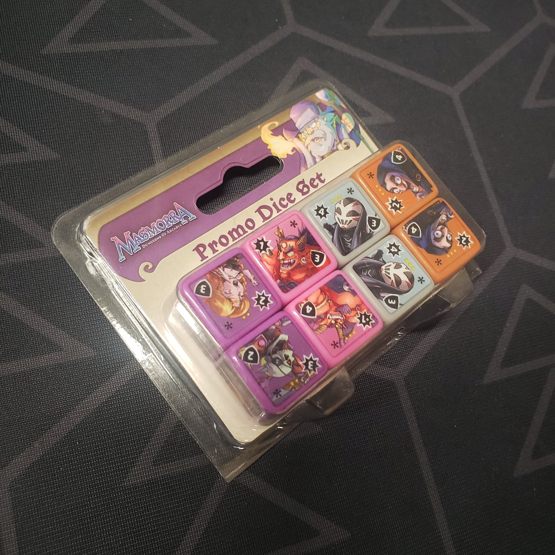 Image shows the front of the packaging of the Promo Dice Set for the board game Masmorra: Dungeons of Arcadia