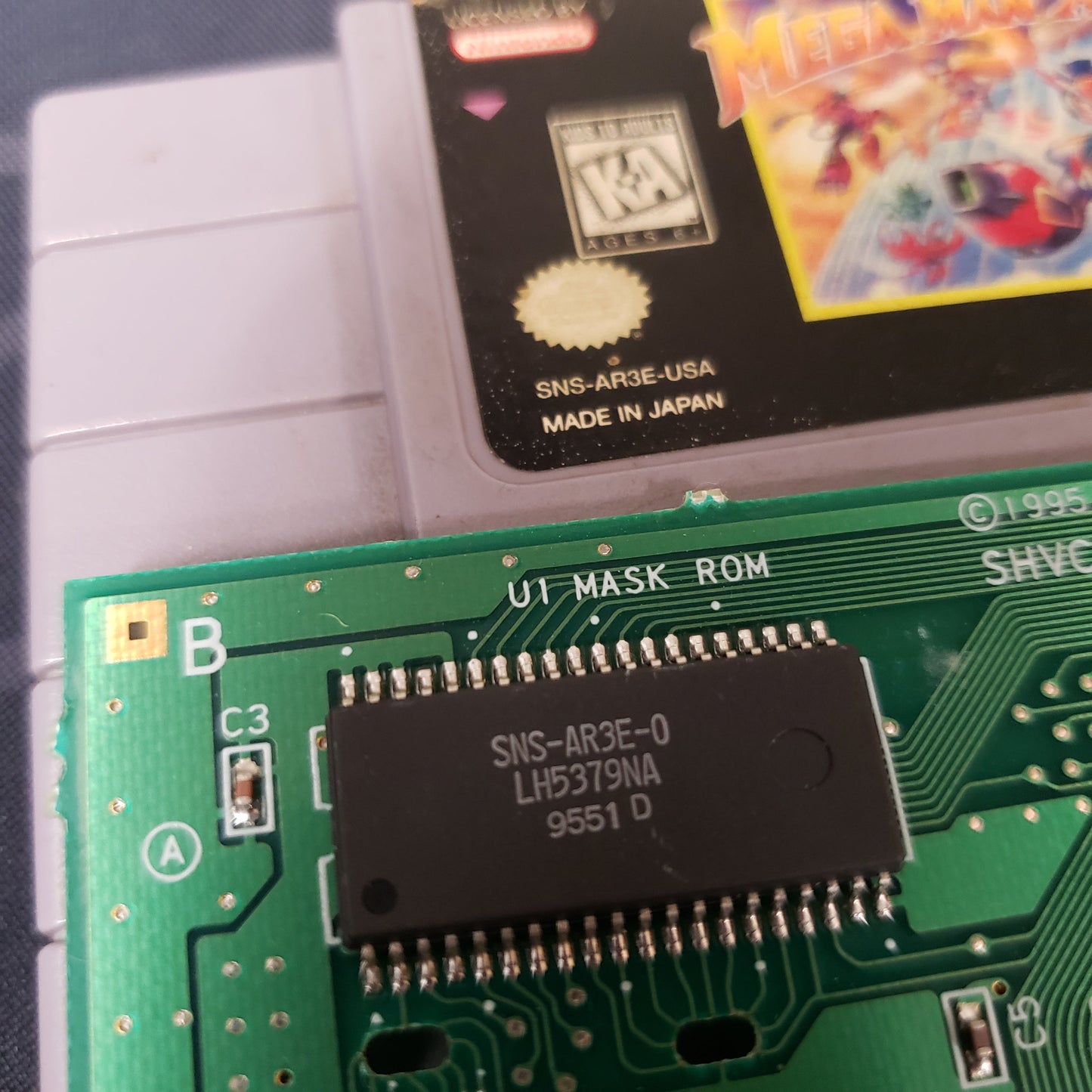 Image shows the program chip on the circuit board next to the front of the cartridge for the video game Mega Man X3