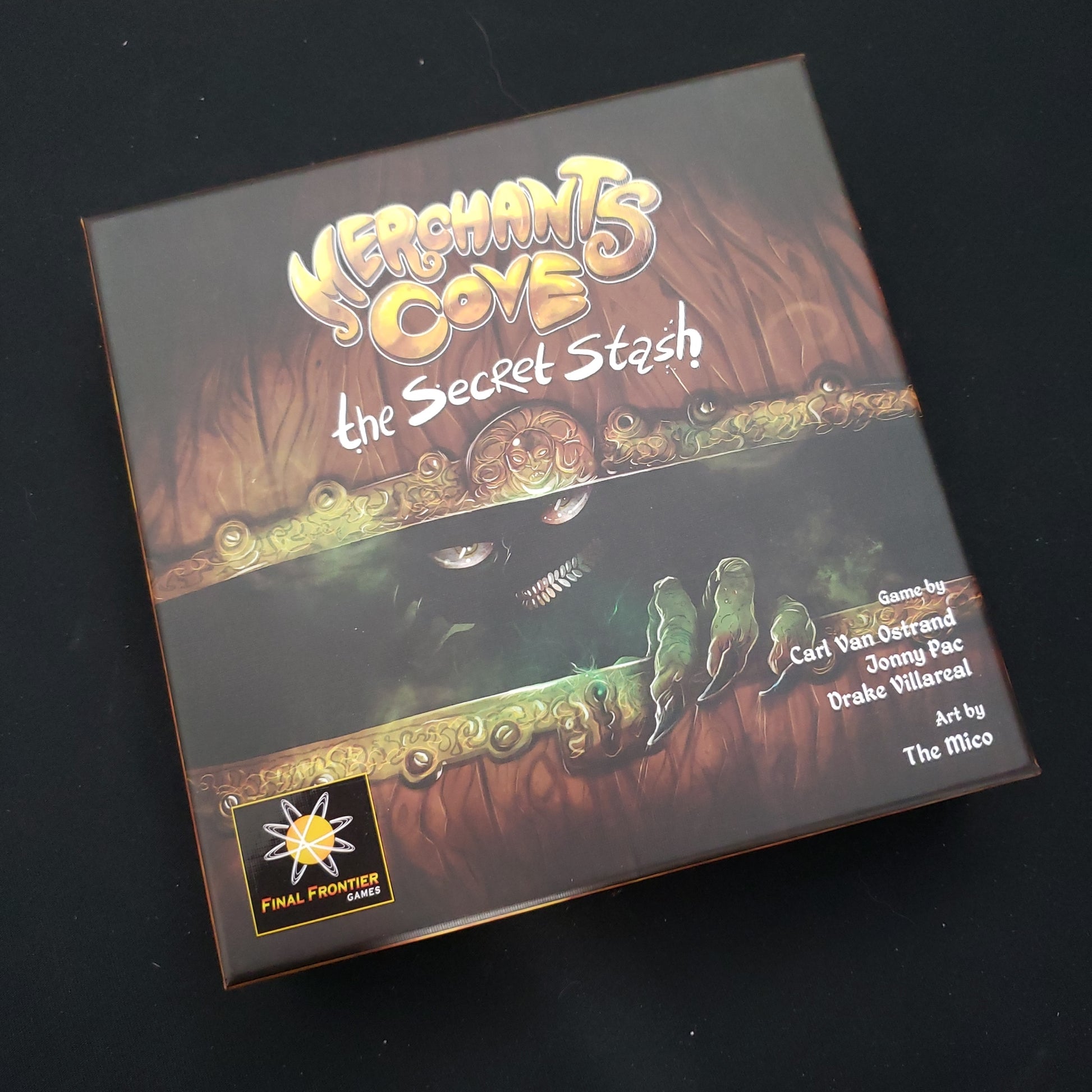 Image shows the front cover of the box of the Secret Stash expansion for the board game Merchants Cove