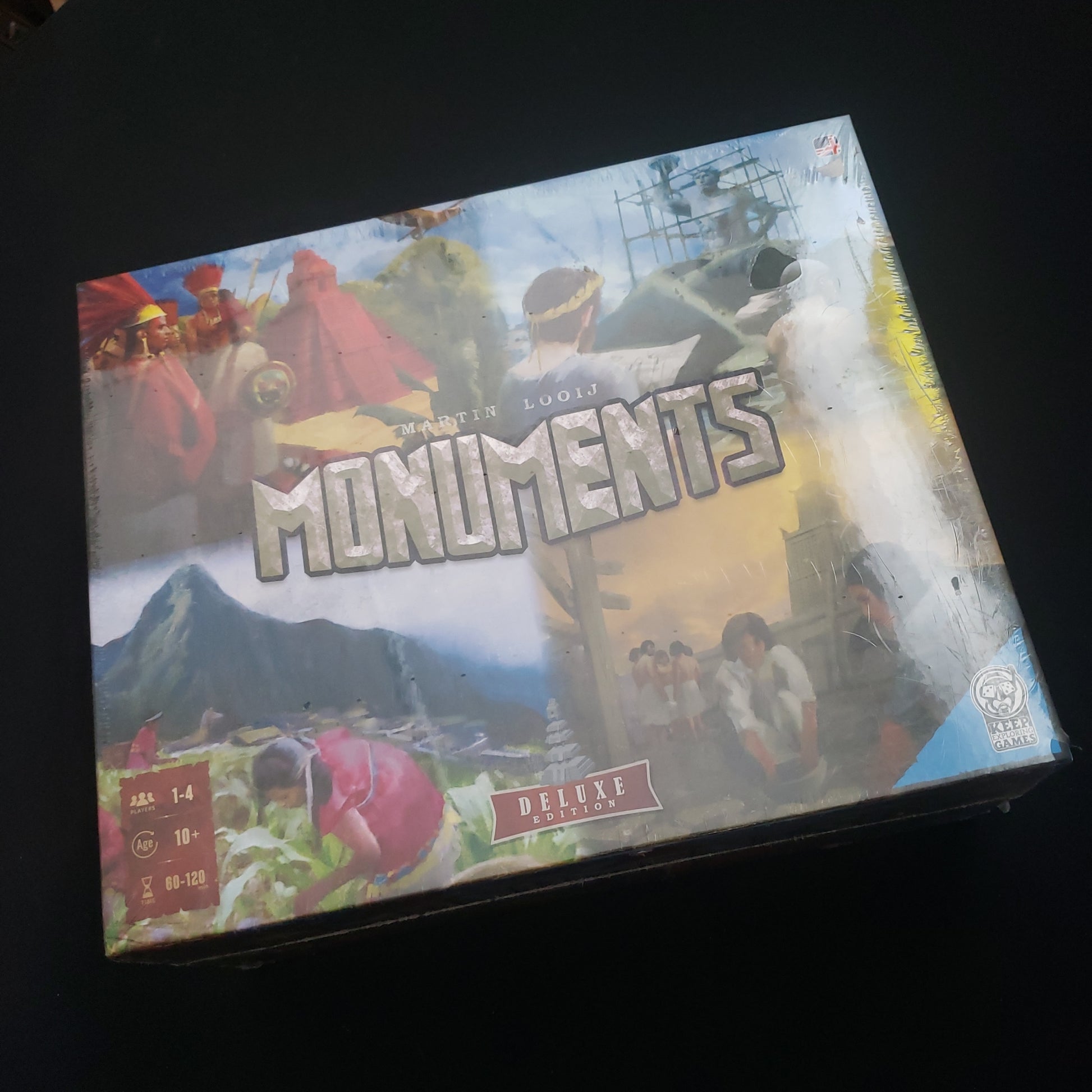 Image shows the front cover of the box of the Monuments: Deluxe Edition board game