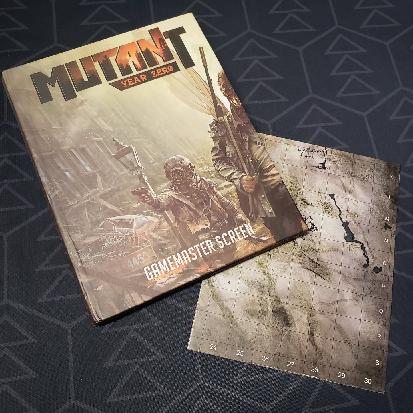Image shows the front panel of the Gamemaster Screen for the roleplaying game Mutant: Year Zero along side a folded map