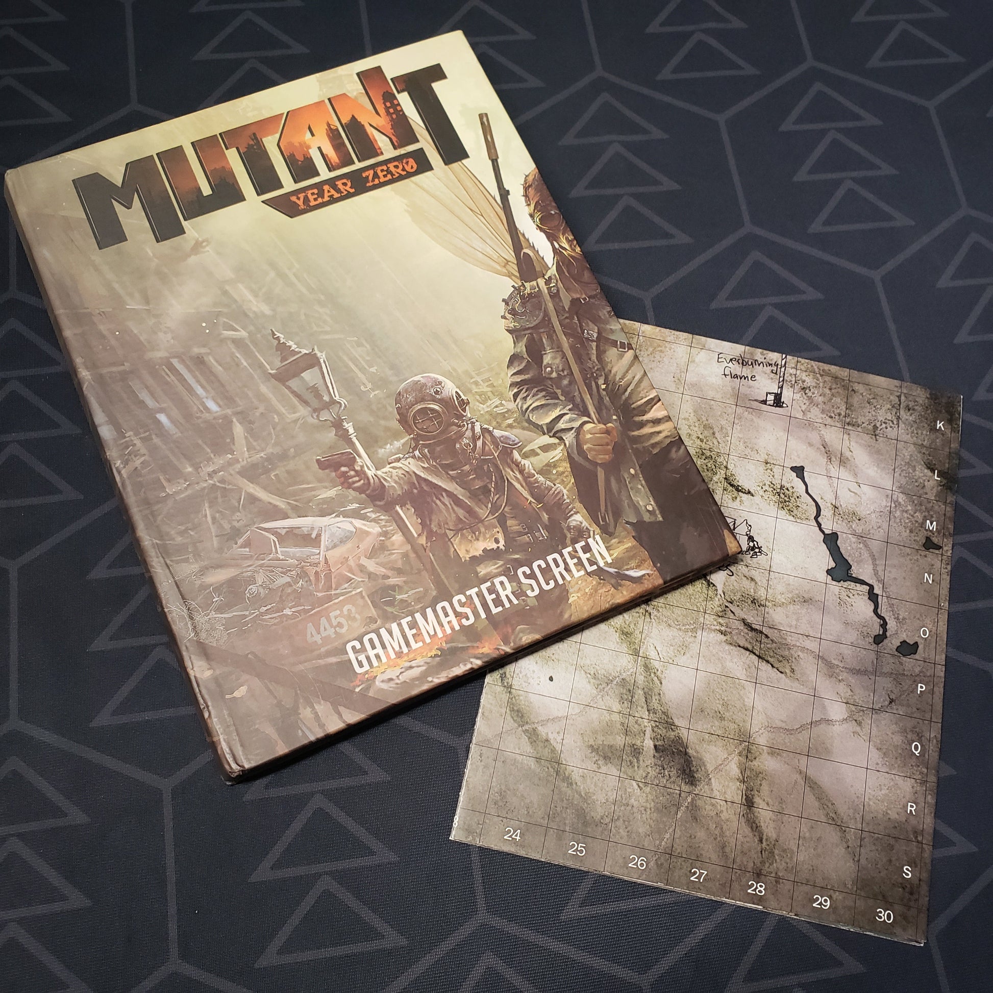 Image shows the front panel of the Gamemaster Screen for the roleplaying game Mutant: Year Zero along side a folded map