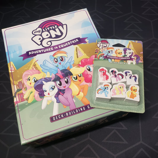 Image shows the front cover of the box of the My Little Pony: Adventures in Equestria Deck-Building Game with the Meeple Pack #1 upgrade sitting on top of it