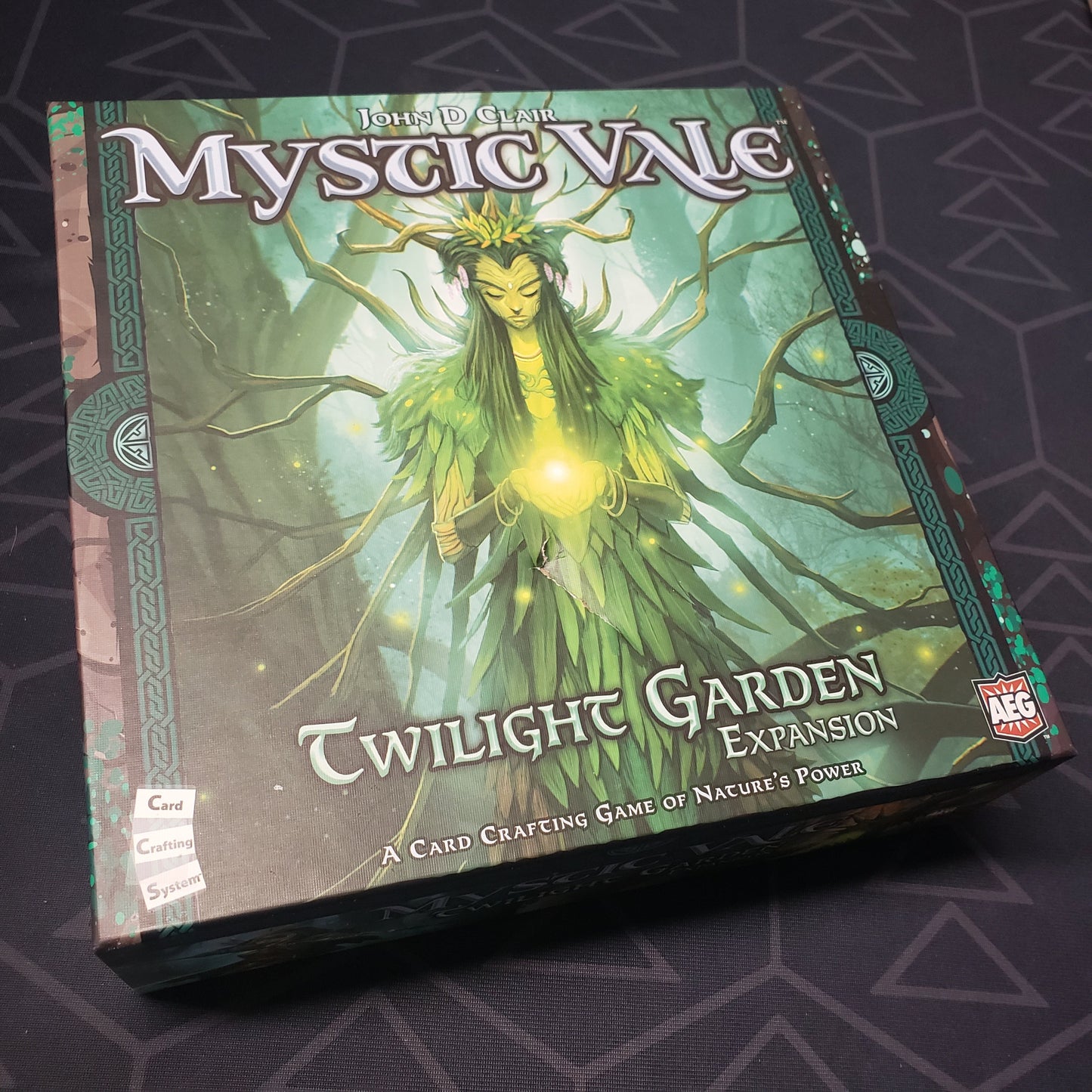 Image shows the front cover of the box of the Twilight Garden expansion for the card game Mystic Vale