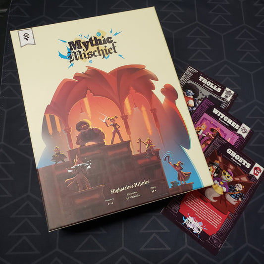 Image shows the front cover of the box for the Mythic Mischief board game sitting op top of the instruction sheets for three expansions