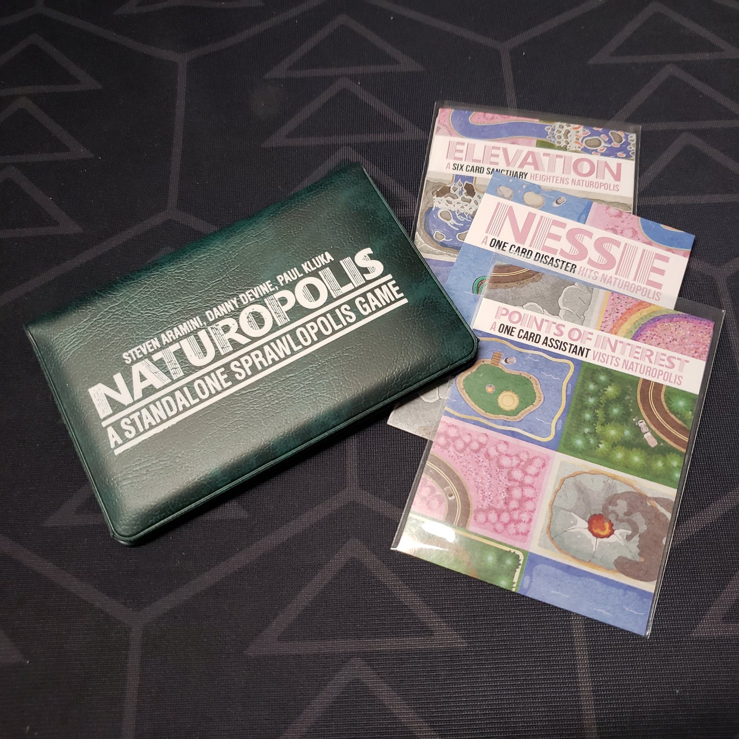 Image shows the front of the card wallet for the Naturopolis card game, with the Nessie, Points of Interest & Elevation expansions sitting next to it
