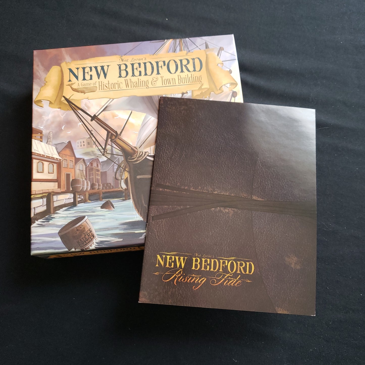 Image shows the front cover of the box of the New Bedford board game, with the instructions for the Rising Tide expansion on top of it