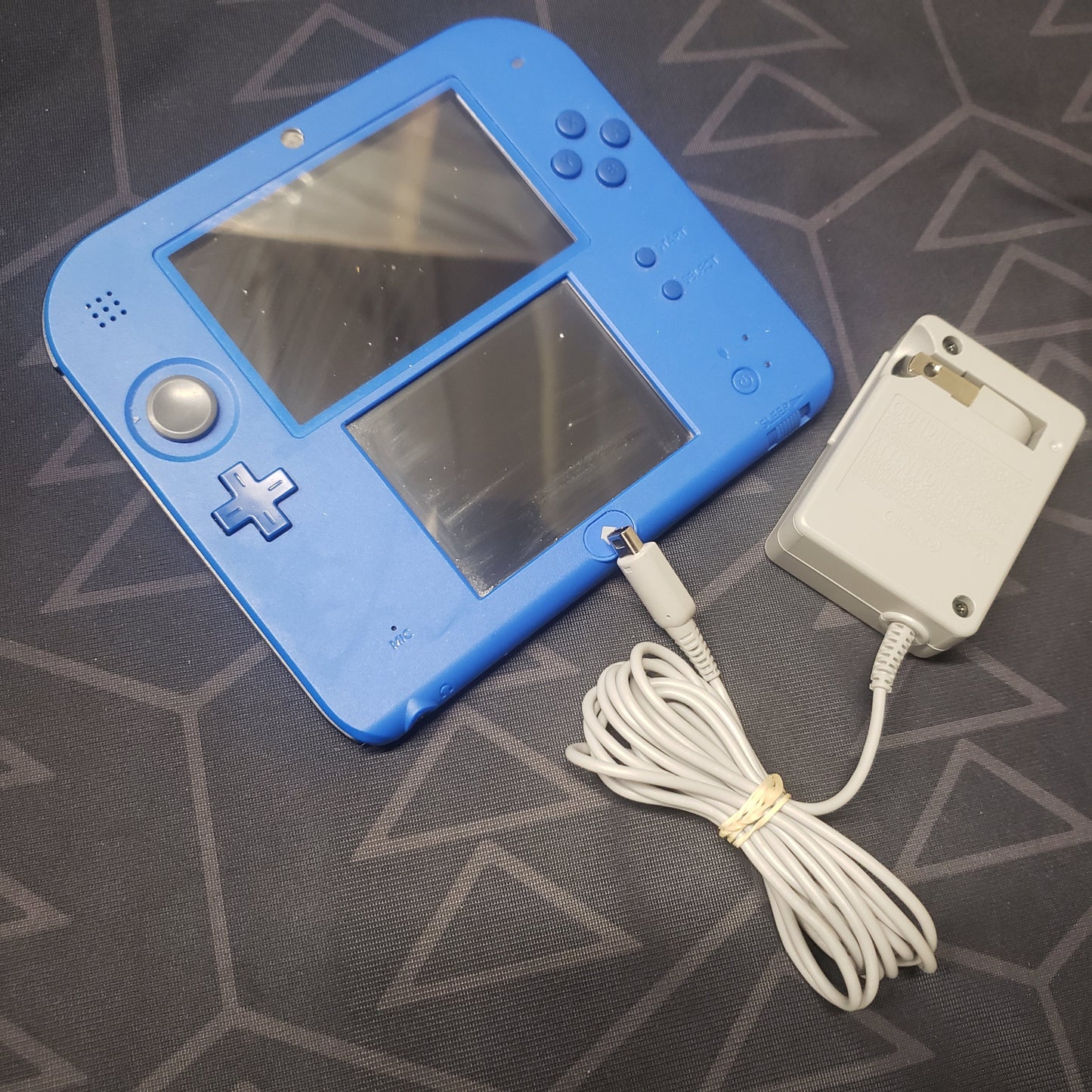 Image shows the front of a Nintendo 2DS Console: Electric Blue 2 (FTR-001) gaming console with the charger sitting next to it