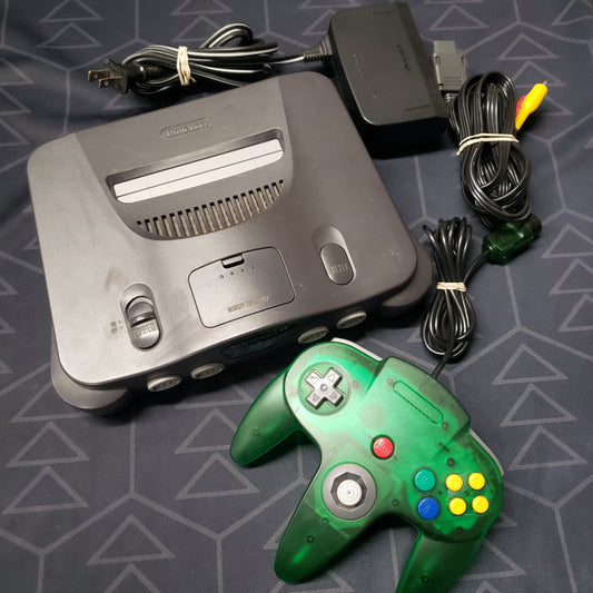 Image shows the top of an Nintendo 64 gaming console surrounded by its cables and a transparent green controller