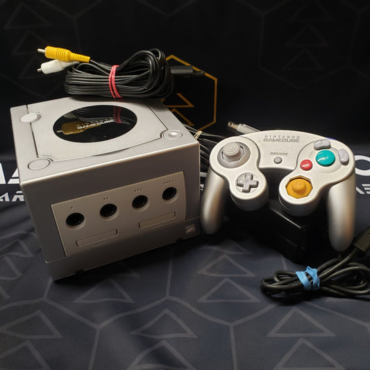 Image shows a platinum color Nintendo GameCube gaming console sitting next to a matching controller with the cables