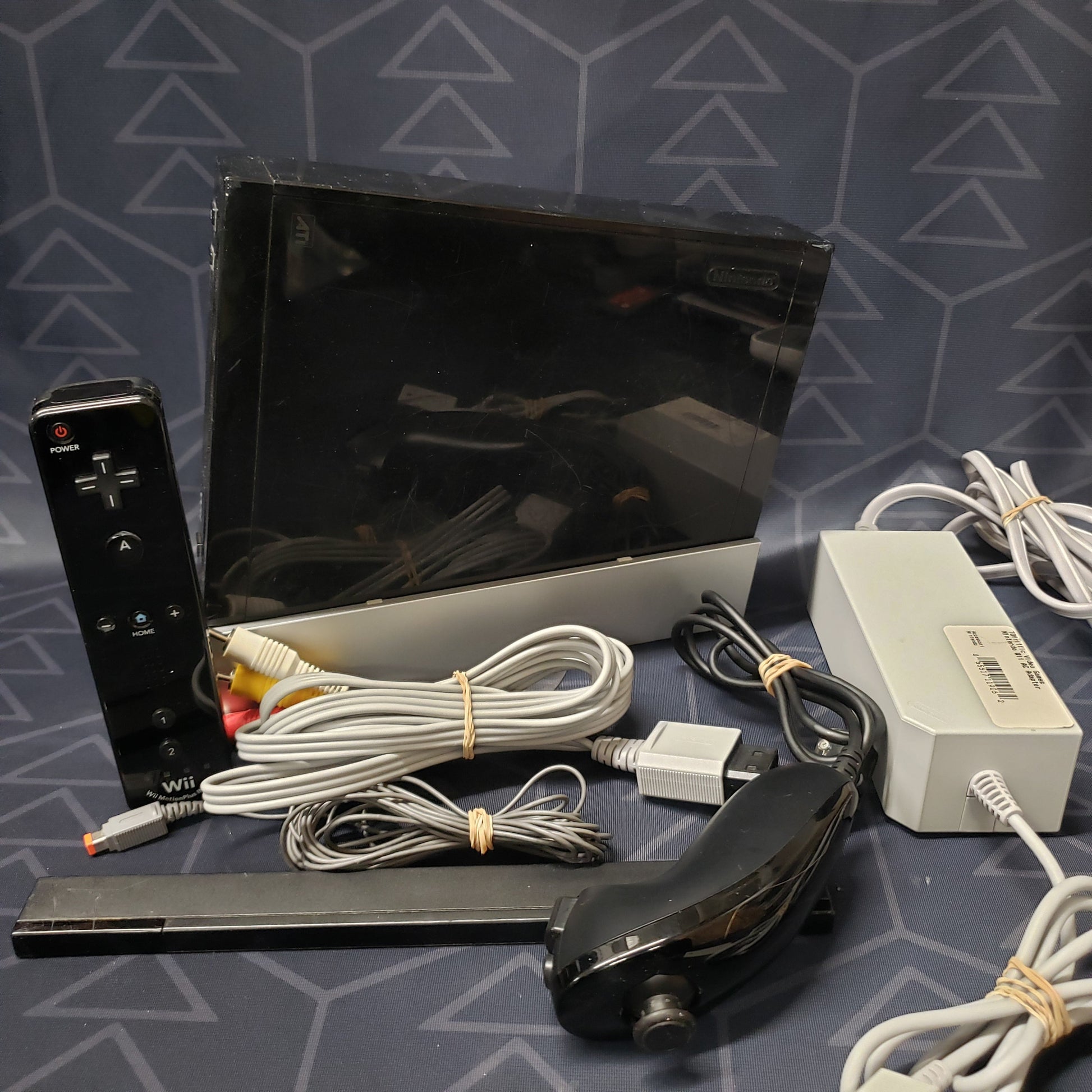 Image shows a black Nintendo Wii console with its controllers & connecting cables laid out
