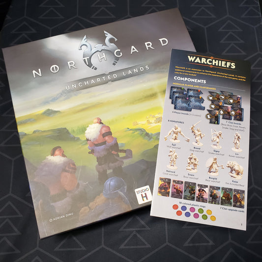 Image shows the front cover of the box of the board game Northgard: Uncharted Lands with the instructions for the Warchiefs expansion sitting on top of it
