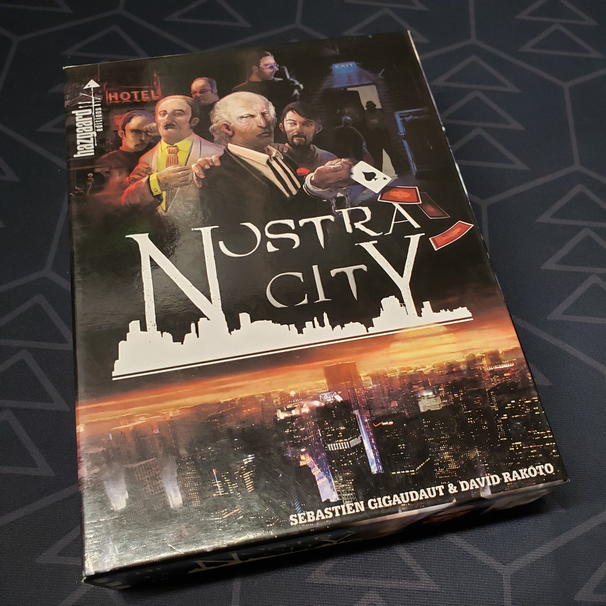 Image shows the front cover of the box of the Nostra City board game