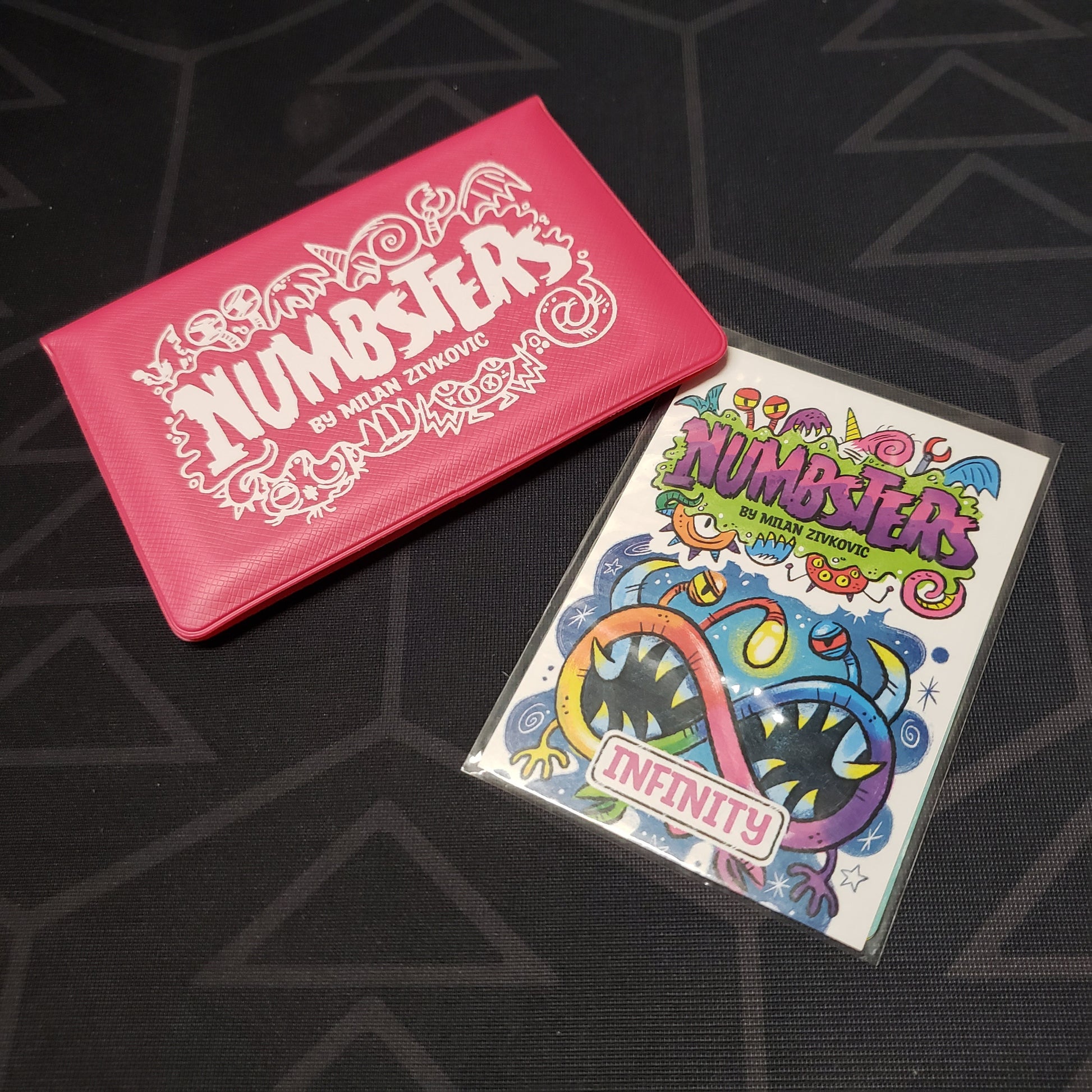 Image shows the front of the card wallet for the Numbsters card game, with the Infinity expansion sitting next to it