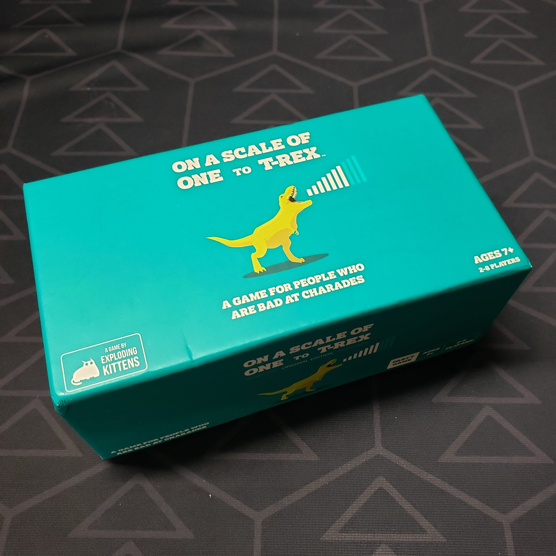 Image shows the front cover of the box of the card game On a Scale of One to T-Rex