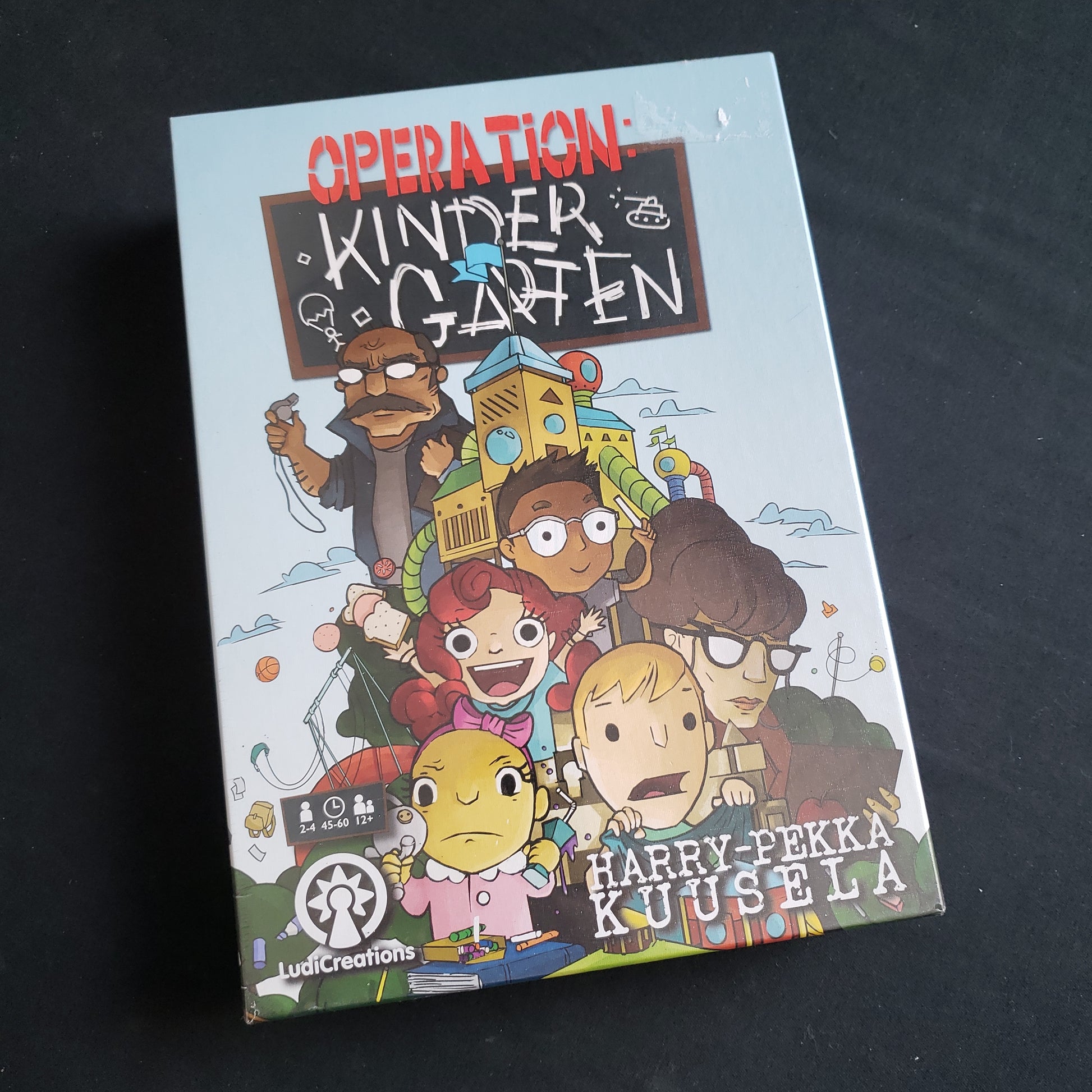 Image shows the front cover of the box of the Operation Kindergarten board game
