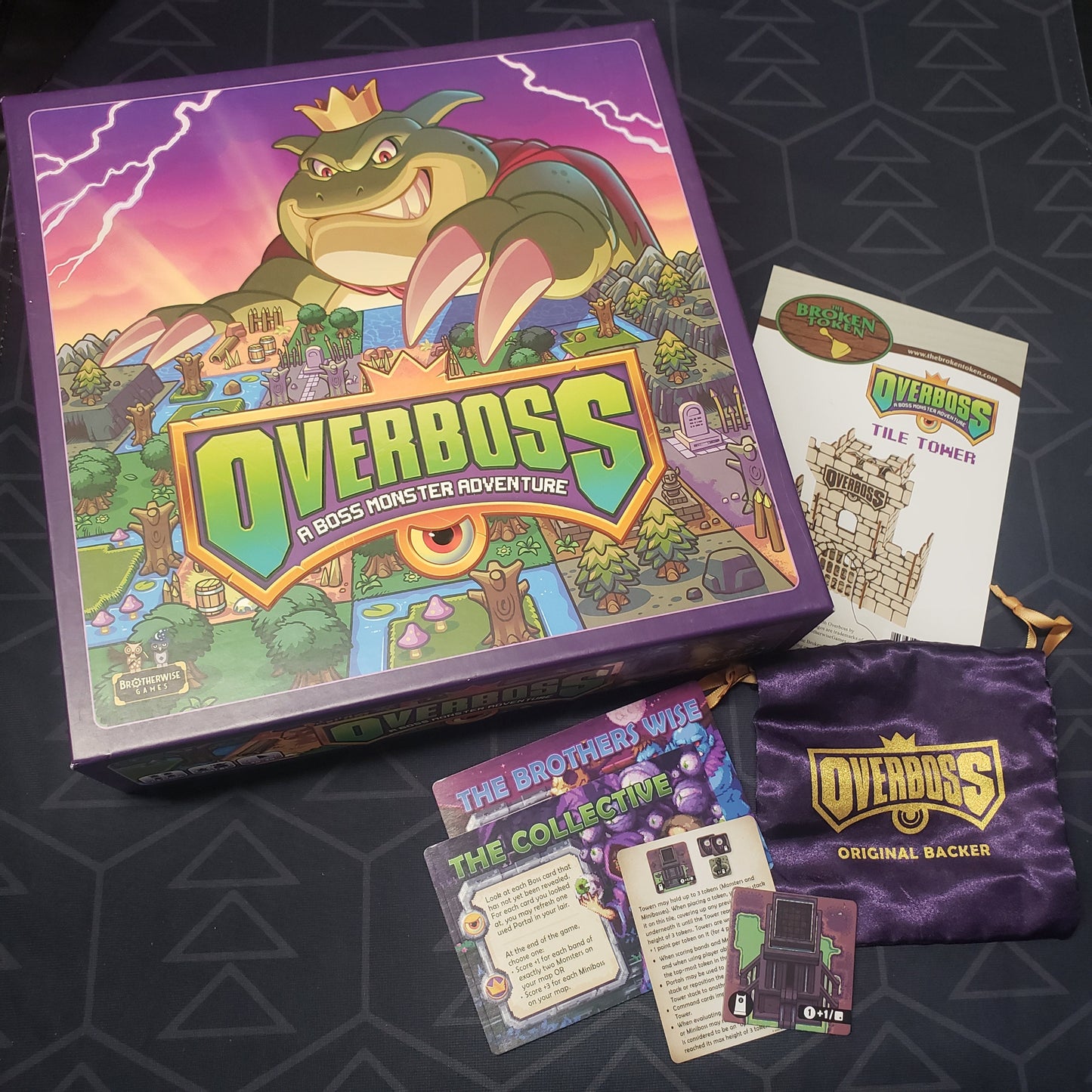 Image shows the front cover of the box of the Overboss board game with the Kickstarter bonus items sitting next to it