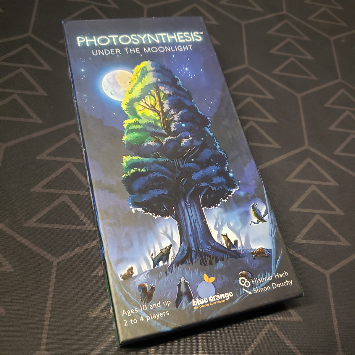 Image shows the front cover of the box of the Under the Moonlight expansion for the board game Photosynthesis