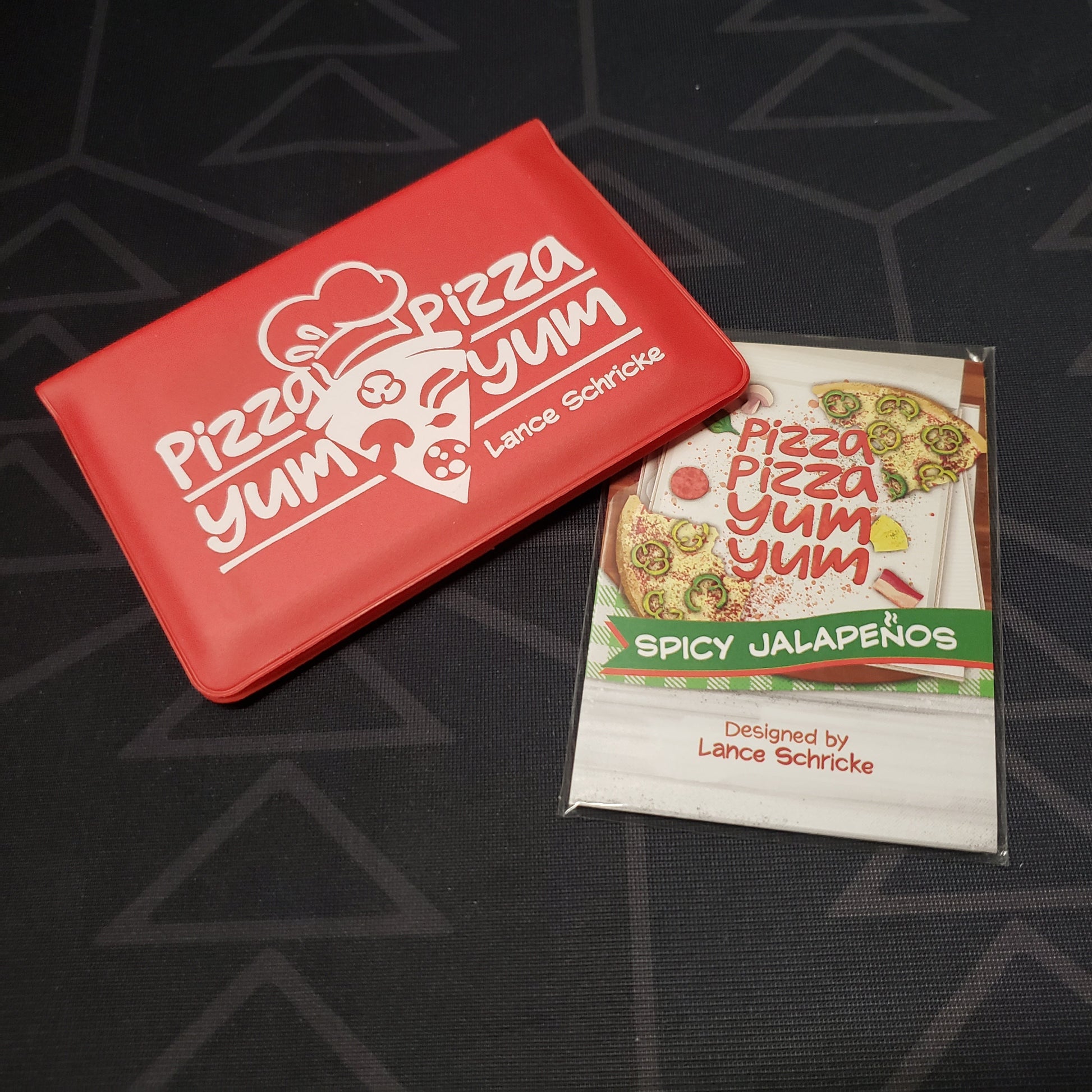 Image shows the front of the card wallet for the Pizza Pizza Yum Yum card game, with the Spicy Jalapenos expansion sitting next to it