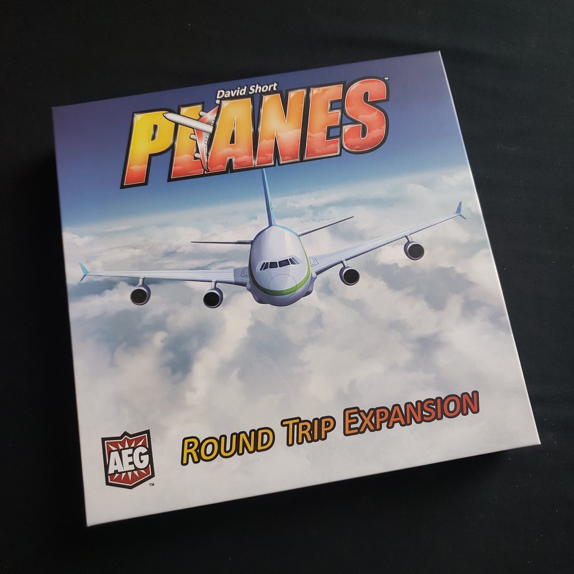 Image shows the front cover of the box of the Round Trip expansion for the Planes board game