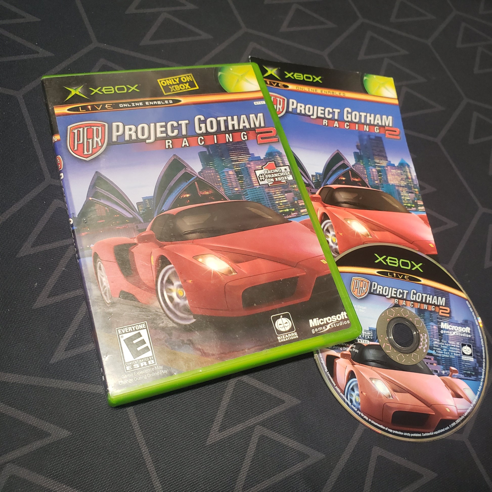 Image shows the case, manual and disc for the video game Project Gotham Racing 2 for the original Xbox