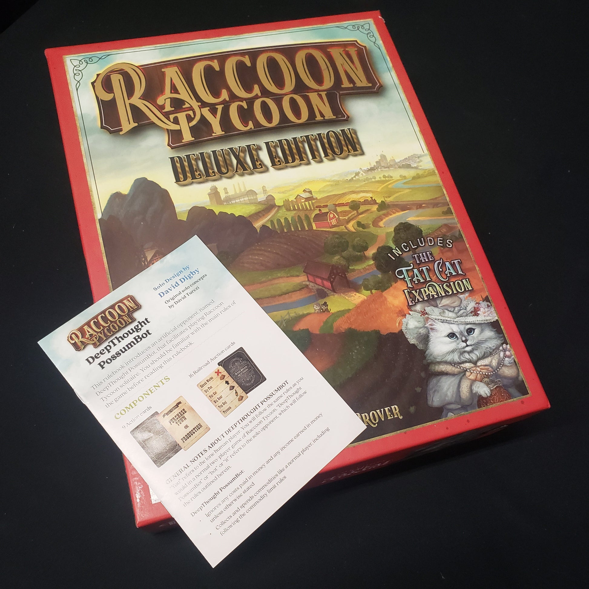 Image shows the front cover of the box for the Raccoon Tycoon: Deluxe Edition board game along with the instructions for the solo mode expansion