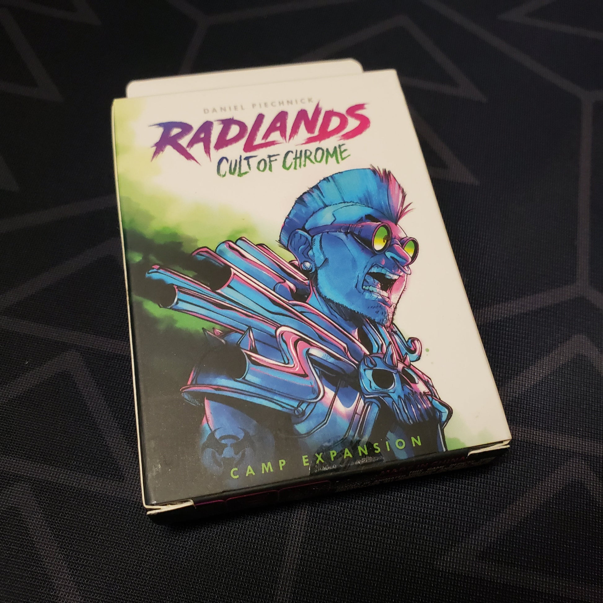 Image shows the front cover of the box of the Cult of Chrome expansion for the card game Radlands