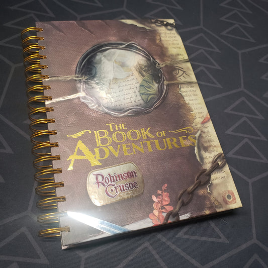 Image shows the front cover of the Book of Adventures scenario expansion book for the board game Robinson Crusoe