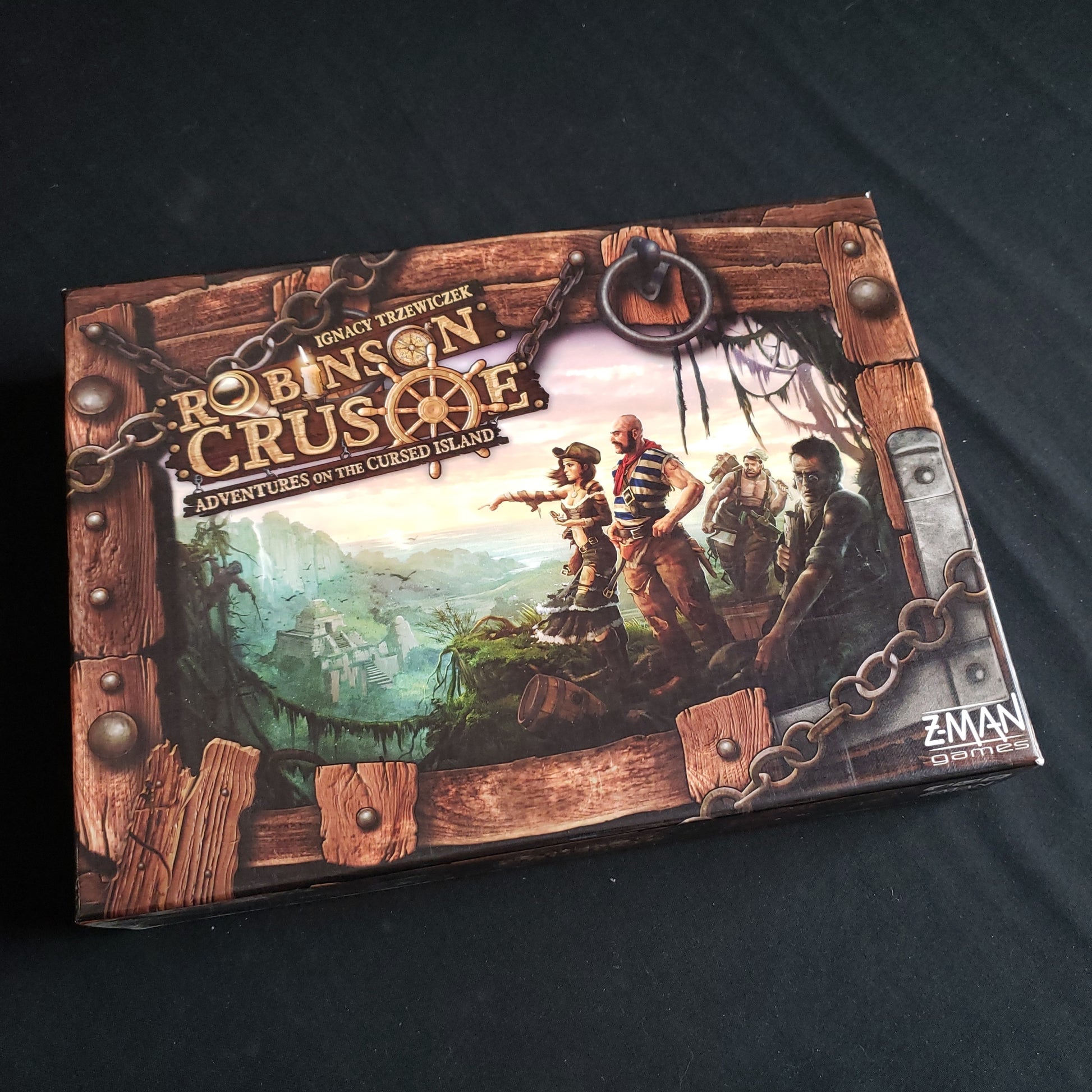 Image shows the front cover of the box of the Robinson Crusoe: Adventures on the Cursed Island board game