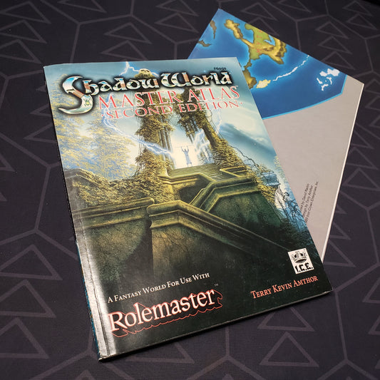 Image shows the front cover of the Shadow World: Master Atlas - Second Edition book for the roleplaying game Rolemaster with the poster map sitting underneath it