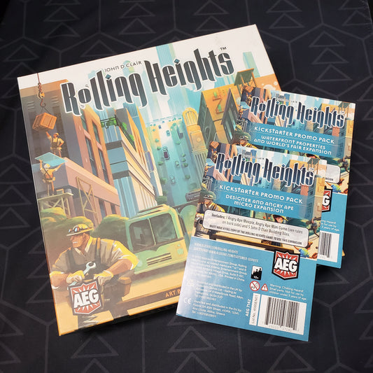 Image shows the front cover of the box of the Rolling Heights board game with the instructions for two Kickstarter promo packs sitting on top of it