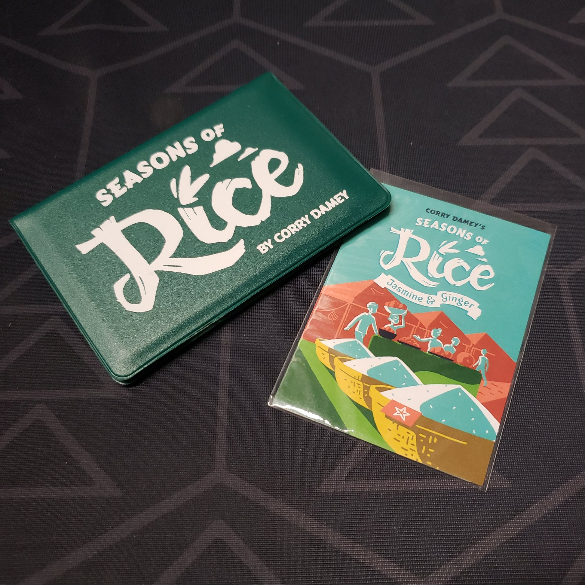 Image shows the front of the card wallet for the Seasons of Rice card game, with the Jasmine & Ginger expansion sitting next to it