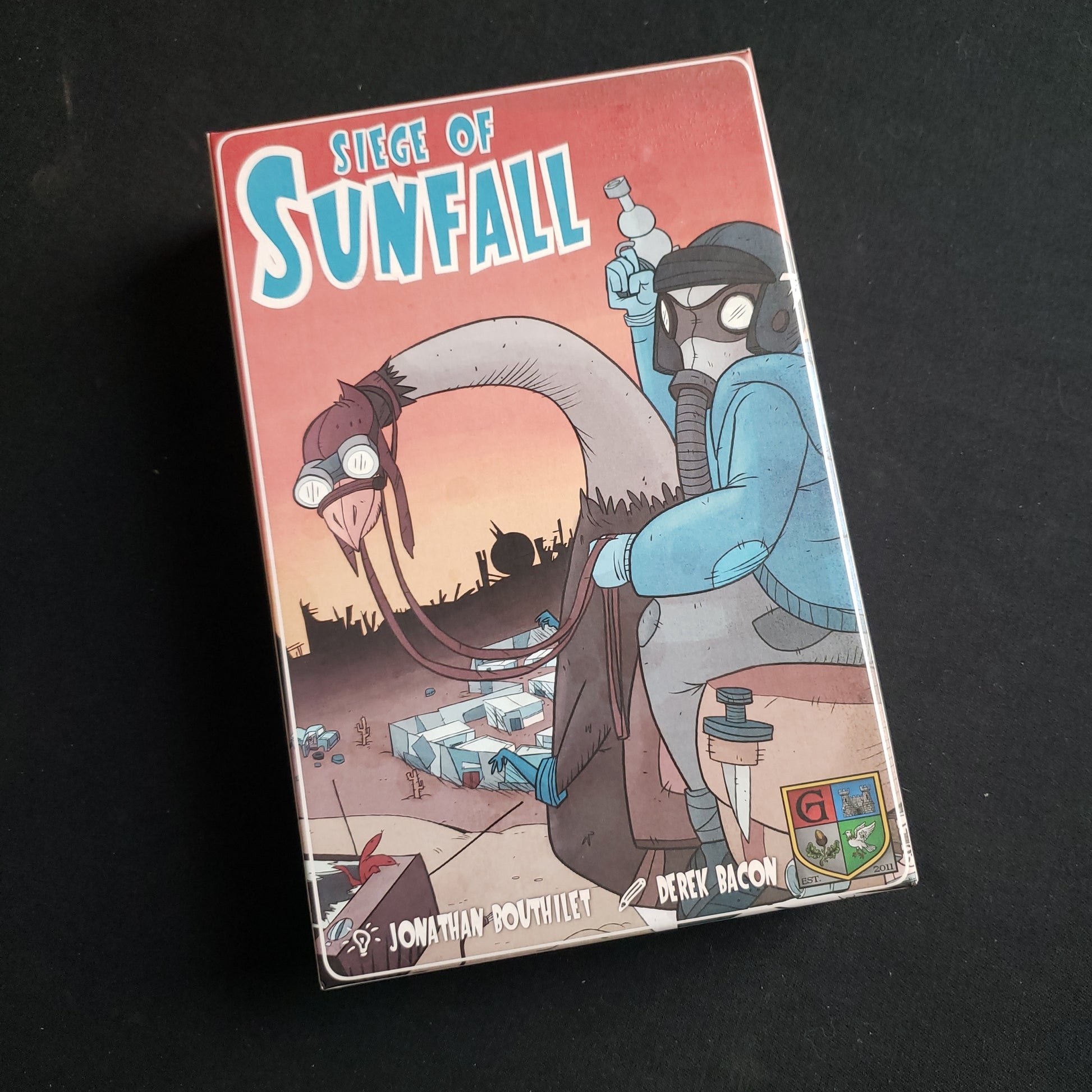 Image shows the front cover of the box of the Siege of Sunfall card game