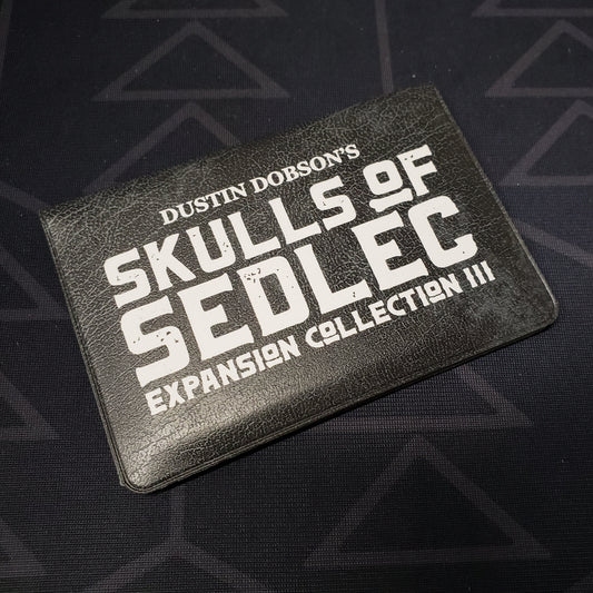 Image shows the front cover of the card wallet of Expansion Collection III for the card game Skulls of Sedlec