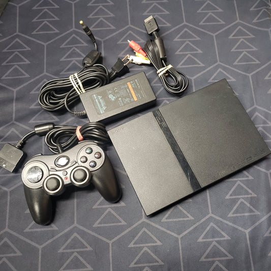 Image shows a black slim Playstation 2 console with a Pelican-brand controller & connecting cables wrapped next to it