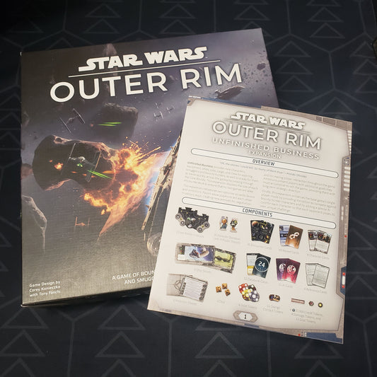 Image shows the front cover of the box of the Star Wars: Outer Rim board game with the instructions for the Unfinished Business expansion sitting on top of it
