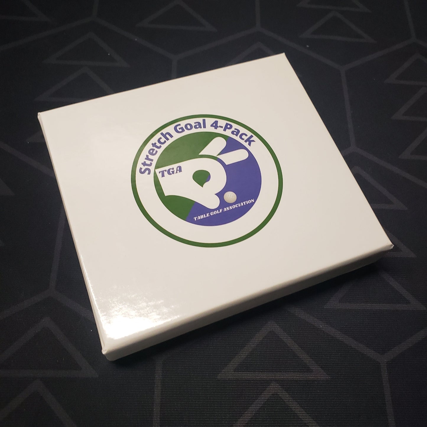 Image shows the front cover of the box of the Stretch Goal 4-Pack expansion for the board game Table Golf Association