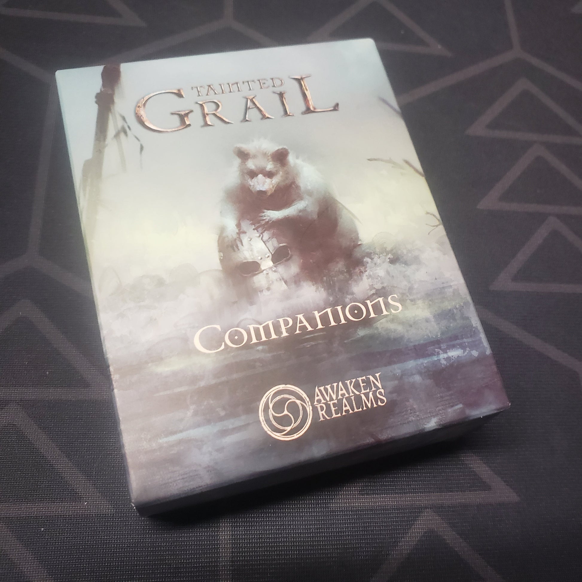 Image shows the front cover of the box of the Companions miniatures expansion for the board game Tainted Grail