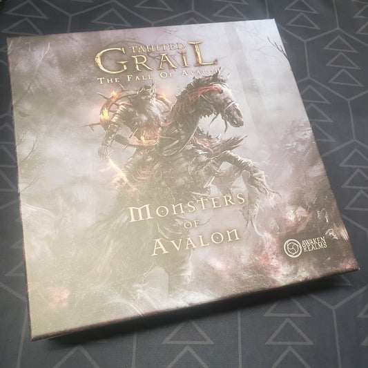 Image shows the front cover of the box of the Monsters of Avalon expansion for the board game Tainted Grail