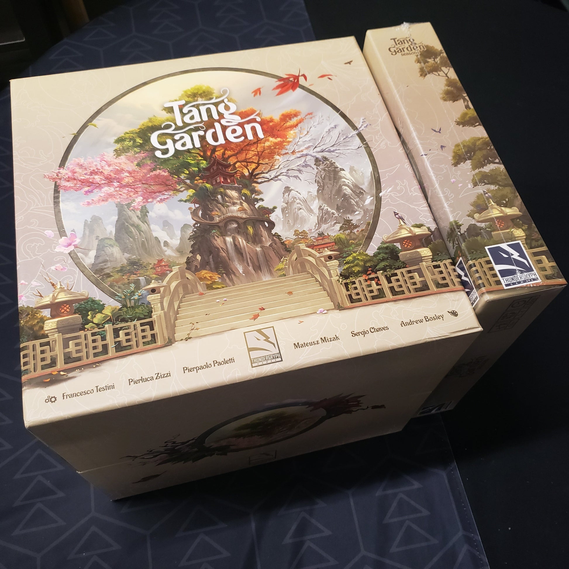 Image shows the top of the Big Box edition for the bpard game Tang Garden, with the sealed Seasons expansion box sitting next to it