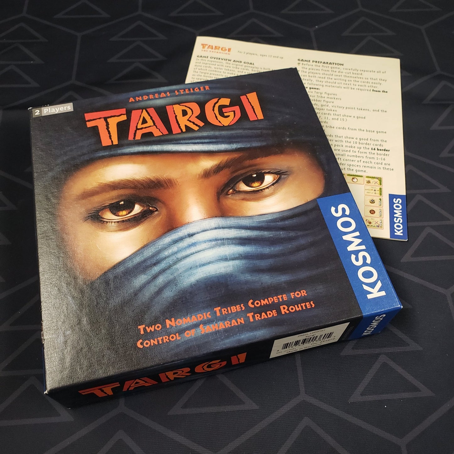 Image shows the front cover of the box of the Targi board game sitting on top of the instructions for the expansion