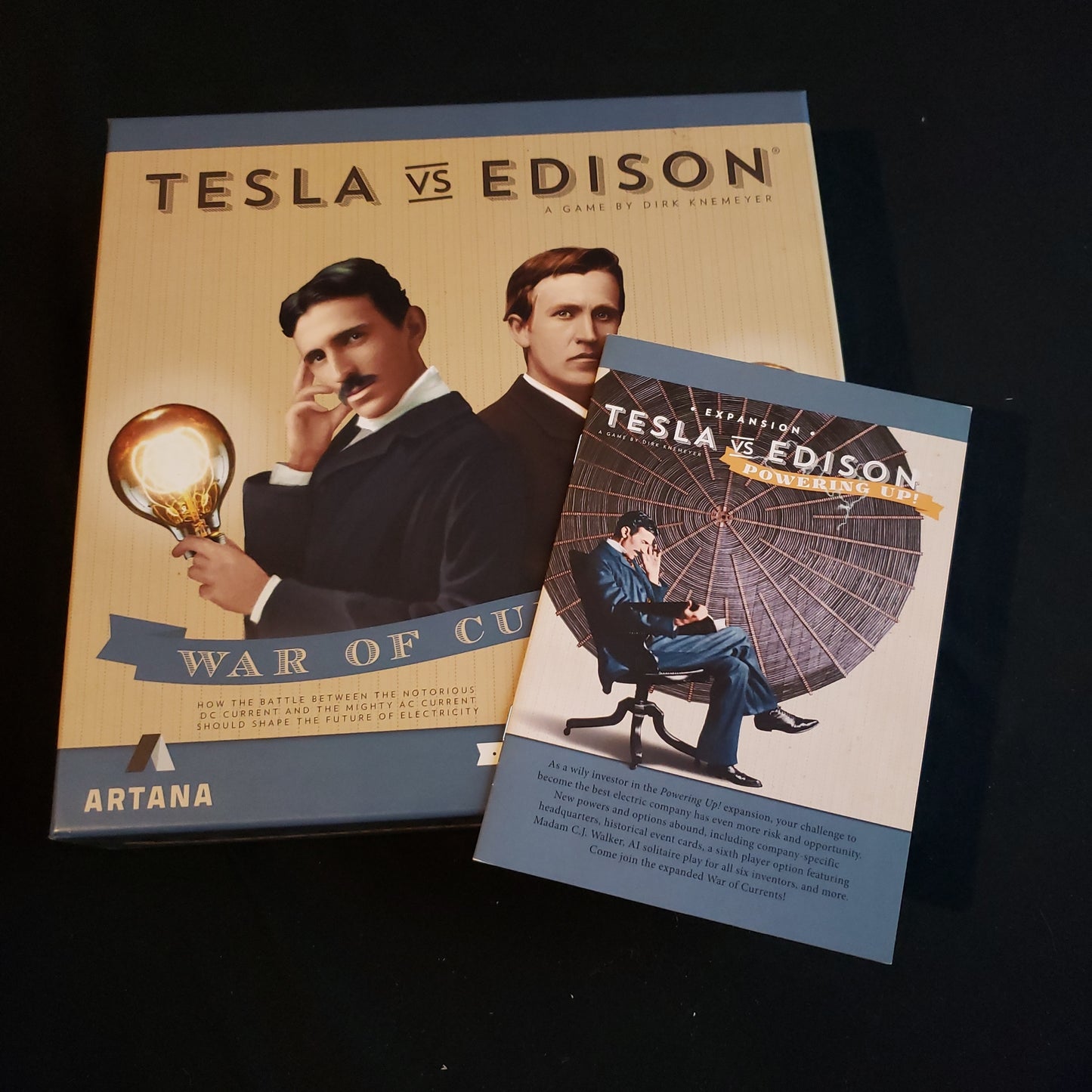 Image shows the front cover of the box of the Tesla vs Edison: War of Currents board game, with the instructions for the Powered Up expansion sitting on top of it