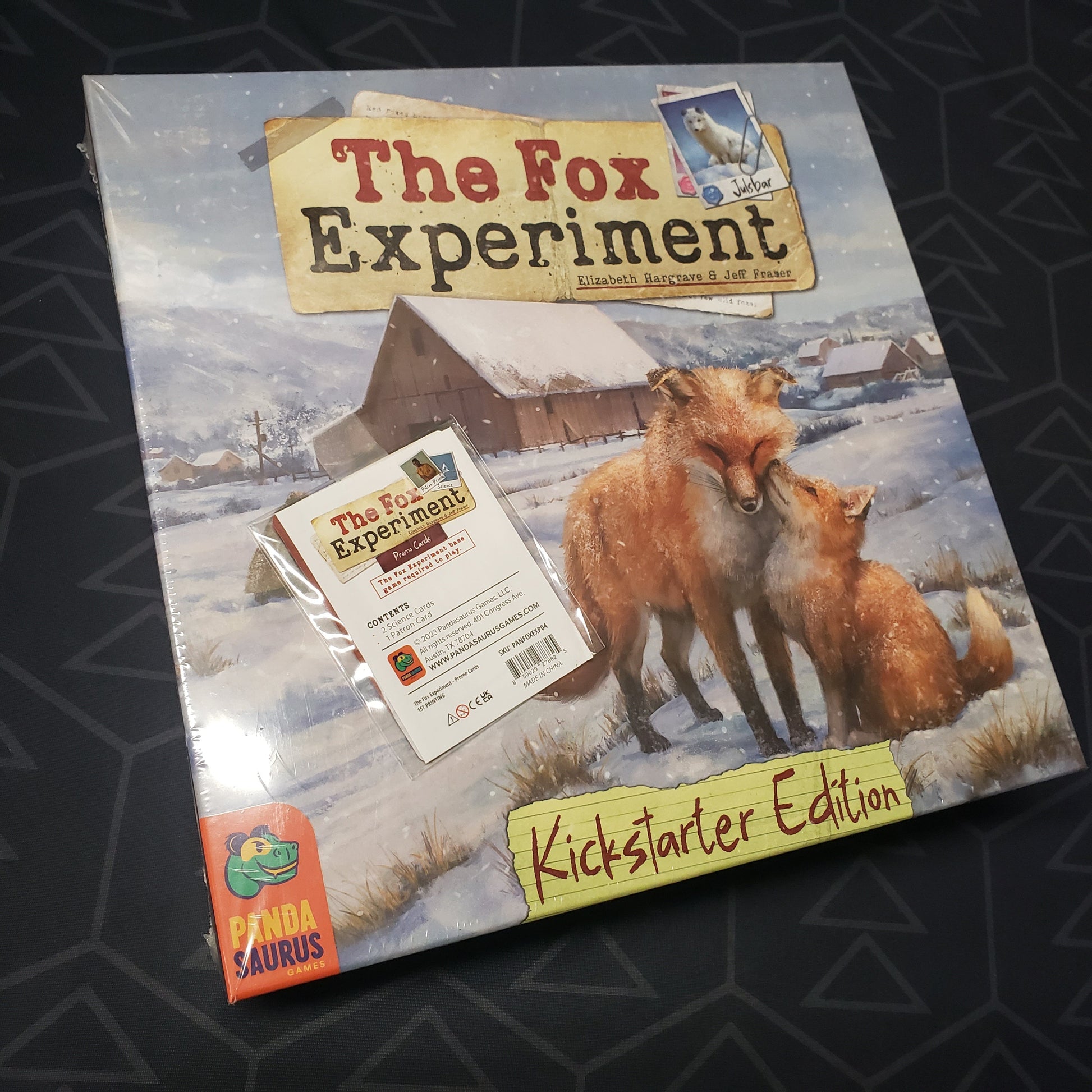 Image shows the front cover of the box for the The Fox Experiment board game with a promo pack of cards taped to it
