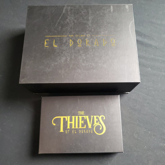 Image shows the front cover of the box of the Island of El Dorado: Legend Edition board game, with the box for the Thieves expansion sitting underneath it
