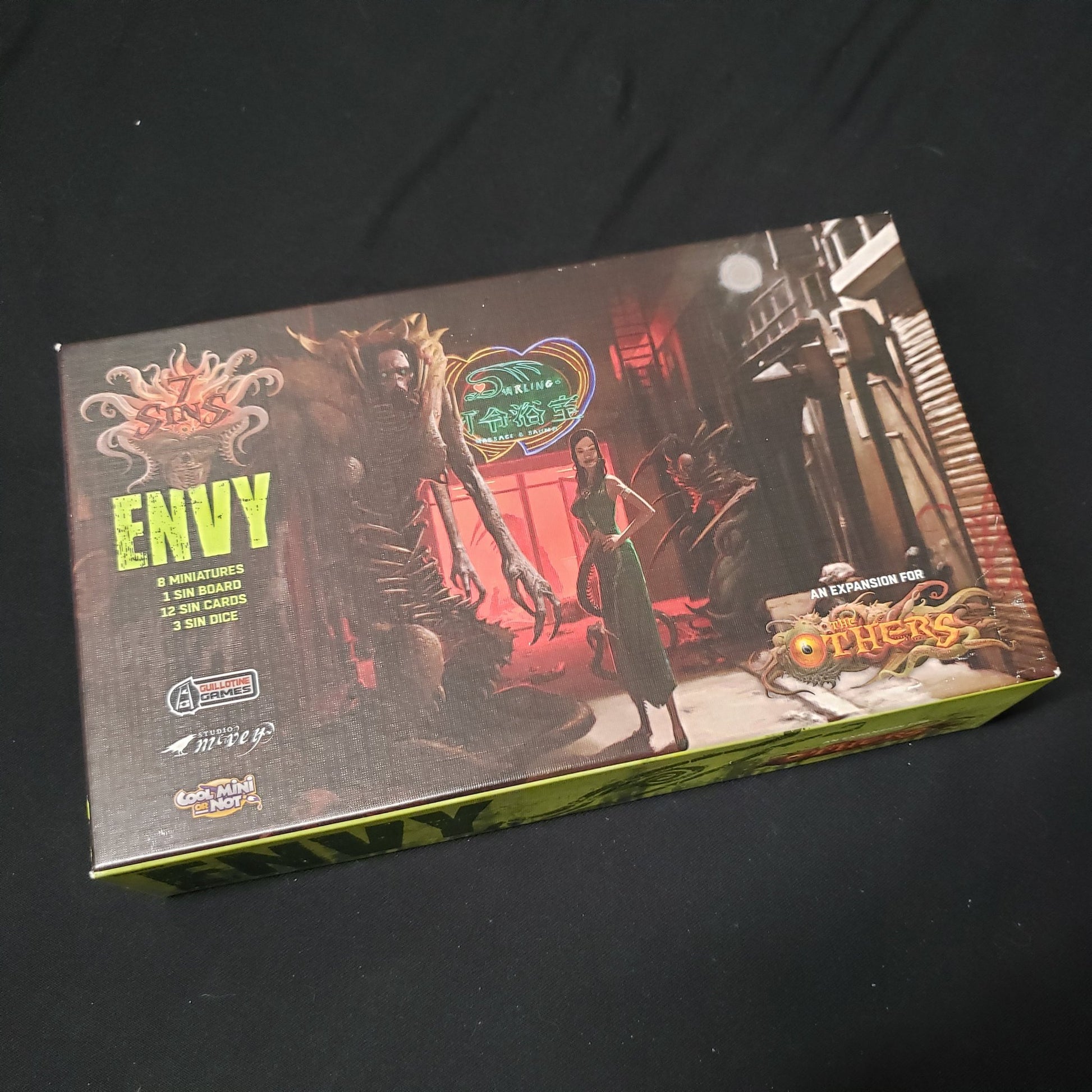 Image shows the front cover of the box of the Envy expansion for the board game The Others